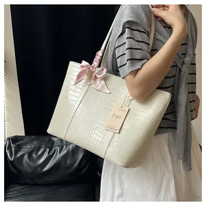Détail du sac cabas crème en cuir crocodile avec une élégante écharpe rose sur l'anse