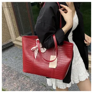 Détail d'un sac cabas rouge à motif crocodile avec un foulard floral rose sur la poignée