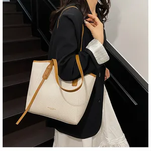 Detail of a large cream tote bag with brown leather handles worn on a shoulder