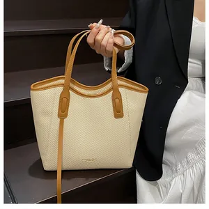 Detail of beige woven tote bag with brown leather handles and adjustable shoulder strap