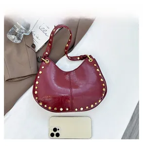 Détail du sac demi-lune rouge brillant avec rivets dorés et téléphone pour comparer la taille