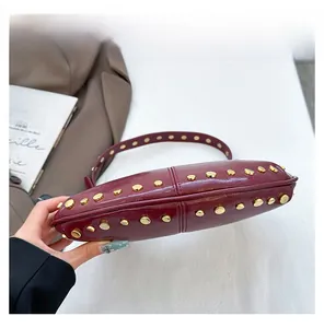 Détail du sac à main en cuir bordeaux avec des rivets dorés et une base surpiquée