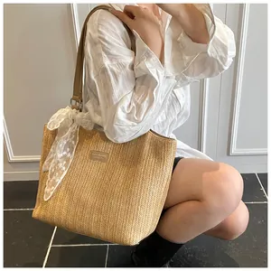 Detail of woven straw tote bag featuring brown faux leather handles and white lace scarf