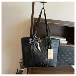 Détail du cabas noir à texture crocodile avec foulard à carreaux sur une étagère