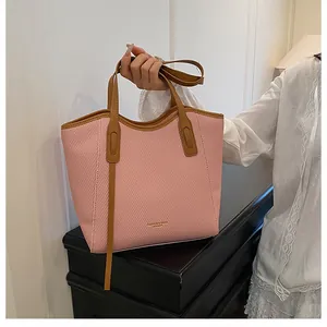 Detail of pink woven tote bag featuring brown leather straps and gold stamped logo