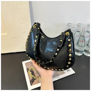 Détail d'un sac à main en cuir noir brillant avec des clous dorés et une chaîne chic