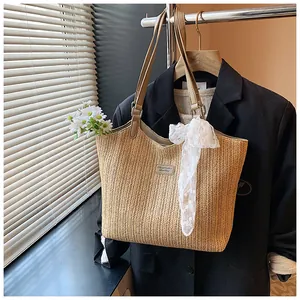 Detail of woven straw tote bag featuring leather shoulder straps and decorative lace ribbon
