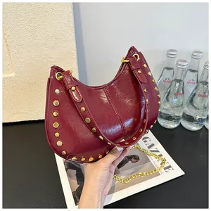Détail du sac à main en cuir verni bordeaux avec des clous métalliques dorés punk