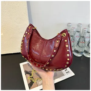 Détail d'un sac à main bordeaux en cuir verni avec clous dorés et bandoulière en chaîne