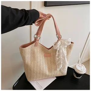 Close-up of a woven straw tote with pink leather handles and white lace scarf detail