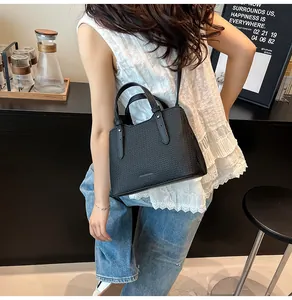 Dettaglio della borsa tote nera a trama intrecciata con tracolla in un caffè urbano