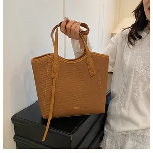 Close-up of brown textured leather tote bag showing fine woven grain and gold logo detail