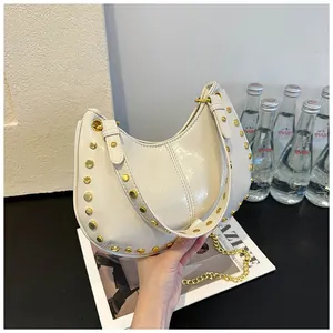 Détail d'un sac à main blanc en demi-lune avec rivets dorés et bandoulière chaîne