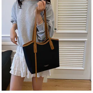 Detail of a large black tote bag with brown leather trim and golden logo lettering