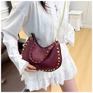 Détail du sac selle bordeaux avec clous dorés et bandoulière sur une robe en dentelle