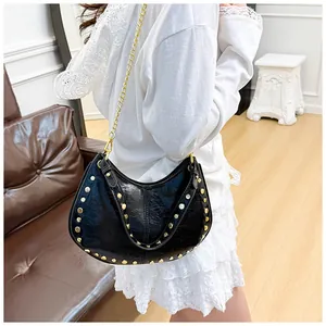 Détail du sac hobo noir avec clous dorés et bandoulière chaîne sur canapé en cuir