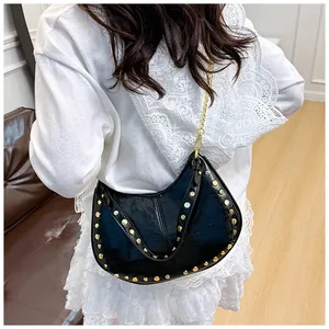 Détail du sac demi-lune noir à rivets avec chaîne dorée sur une robe blanche
