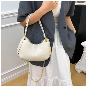 Détail d'un sac lune beige avec clous dorés et chaîne en métal sur un mannequin