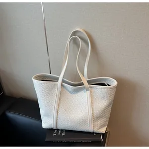 Detailed close-up of a white woven texture tote bag with slim shoulder straps on a table