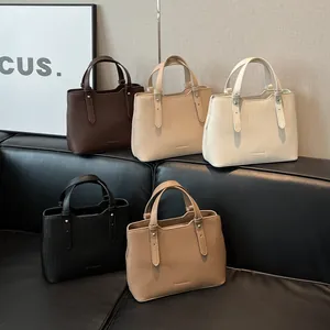 Borse tote minimaliste in ecopelle in cinque colori esposte su un divano in pelle nera