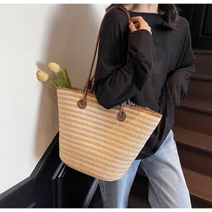Detail of woven straw tote bag with brown leather straps and fringed edge on model