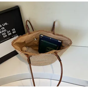 Large straw woven tote bag with brown leather handles and fringe detail for beach or travel