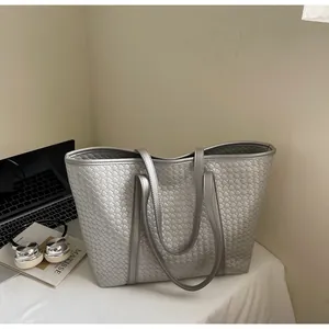 Detail of silver tote bag with woven texture, headphones and laptop on a desk