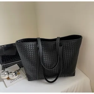 Detail shot of the black woven texture and leather handles of a large tote bag