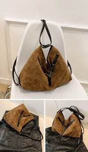 Detalle de un bolso tote de ante marrón con asas de cuero negro y herrajes dorados