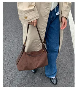 Detail view of a brown faux suede tote bag with a dark leather strap on a street background