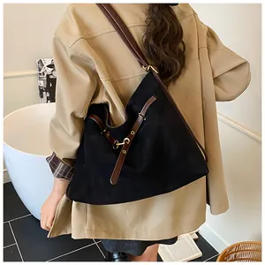 Detail of a large black suede tote bag with brown leather strap worn by a model