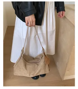 Detail of a large khaki faux suede tote bag with a soft plush ball charm on a model