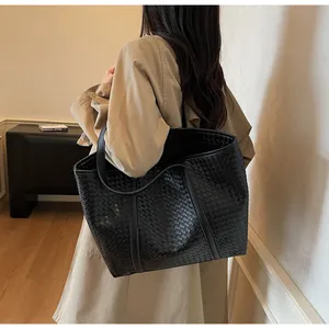 Detail view of a large black woven leather tote bag with thick shoulder straps
