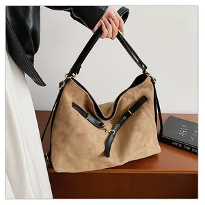 Detalle de bolso tote de ante marrón con correas de cuero negro y hebillas doradas retro