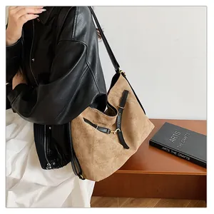 Detalle de bolso tote de ante marrón con correas de cuero negro y hebillas metálicas