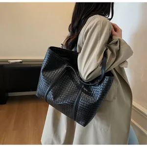 Detail of black woven tote bag with slim shoulder straps on a beige trench coat