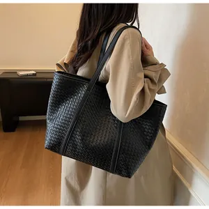 Detail of a large black woven tote bag with leather straps on a model in a trench coat
