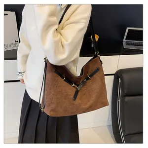 Detalle de bolso tote de ante marrón con correas de cuero negro en V y hebillas doradas