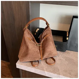 Detail of a brown suede tote bag featuring smooth leather straps and vintage metal buckles