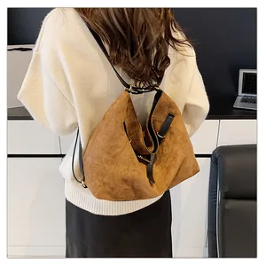 Detalle de bolso de ante marrón con correa de cuero negro y hebillas metálicas doradas