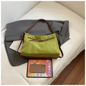 Detail of green suede tote bag showing brown leather straps and metallic buckle accent