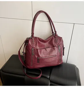 Close-up of wine red leather handbag featuring functional zippers and silver metal rivets