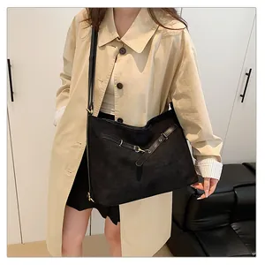 Detalle del bolso tote de ante negro con hebilla metálica sobre una gabardina clásica