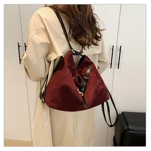 Detalle del bolso tote de gamuza burdeos con correas de cuero negro y herrajes de oro