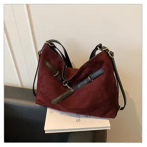 Detalle del bolso tote de ante burdeos con correas de cuero negro y herrajes dorados