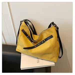 Detalle del bolso tote de ante amarillo con correas de cuero negro y metal dorado