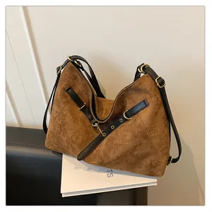 Detalle de bolso tote de gamuza marrón con correas de cuero negro y herrajes dorados