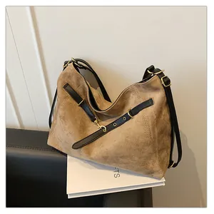 Detalle de un bolso tote grande de ante marrón con asas de cuero negro y herrajes dorados