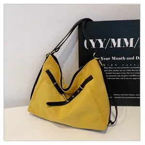 Detalle de bolso tote de ante amarillo con correa negra y detalles metálicos dorados