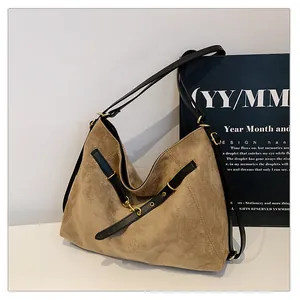 Detalle del bolso tote de ante caqui con correas de cuero negro y herrajes dorados